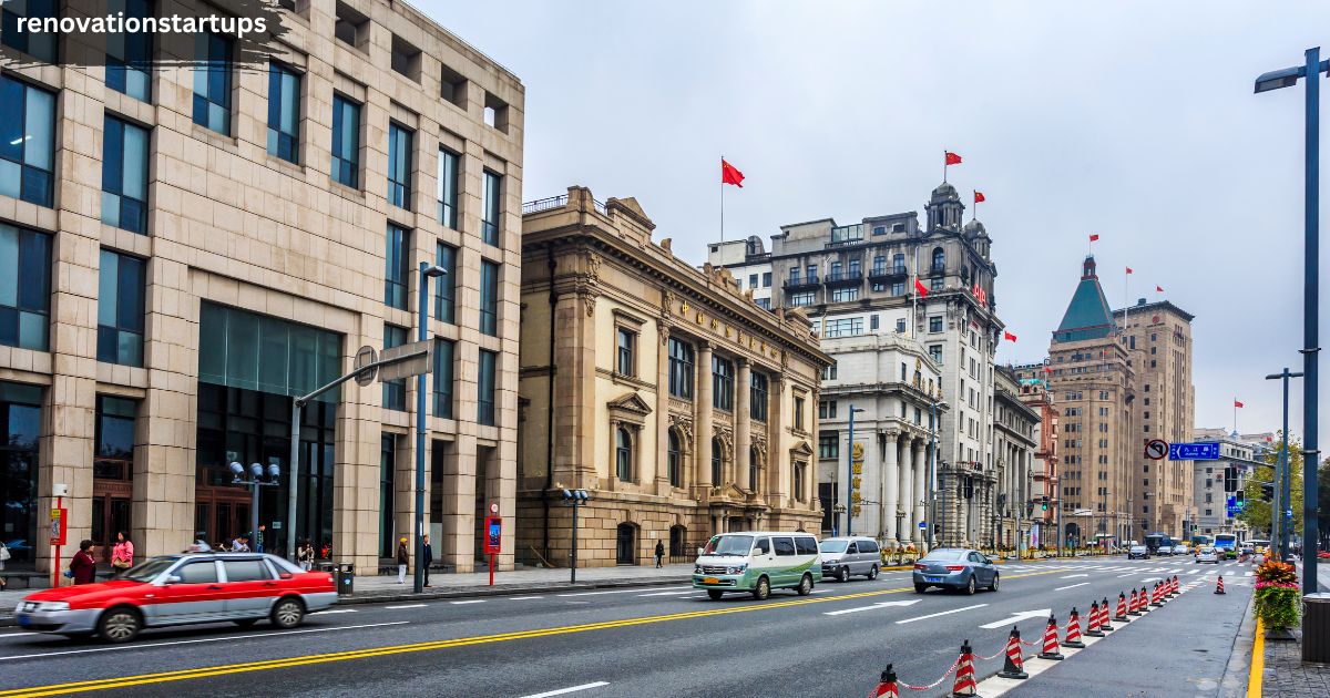 Historic colonial-style buildings along a busy city street with Chinese flags, traffic cones, and cars driving past