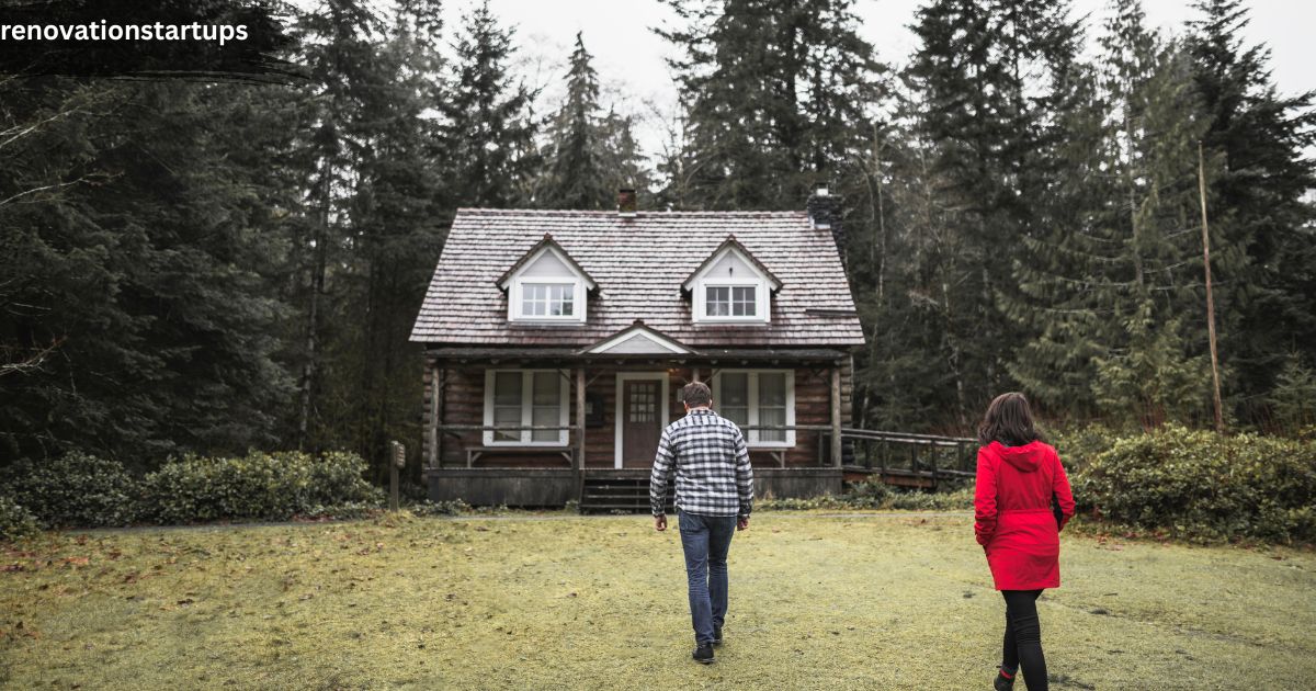 A rustic two-story house nestled near a dense forest, featuring a traditional wooden shingle roof and clean white dormer windows. A couple is walking across the green grass lawn toward the front entrance of the home, illustrating the real-life journey of renters exploring or touring potential houses to rent near me.