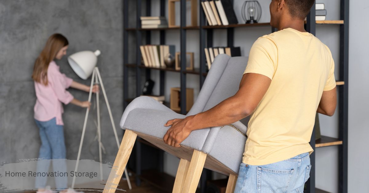 Couple carrying a grey armchair and floor lamp to a bookshelf area during home renovation storage and furniture setup.