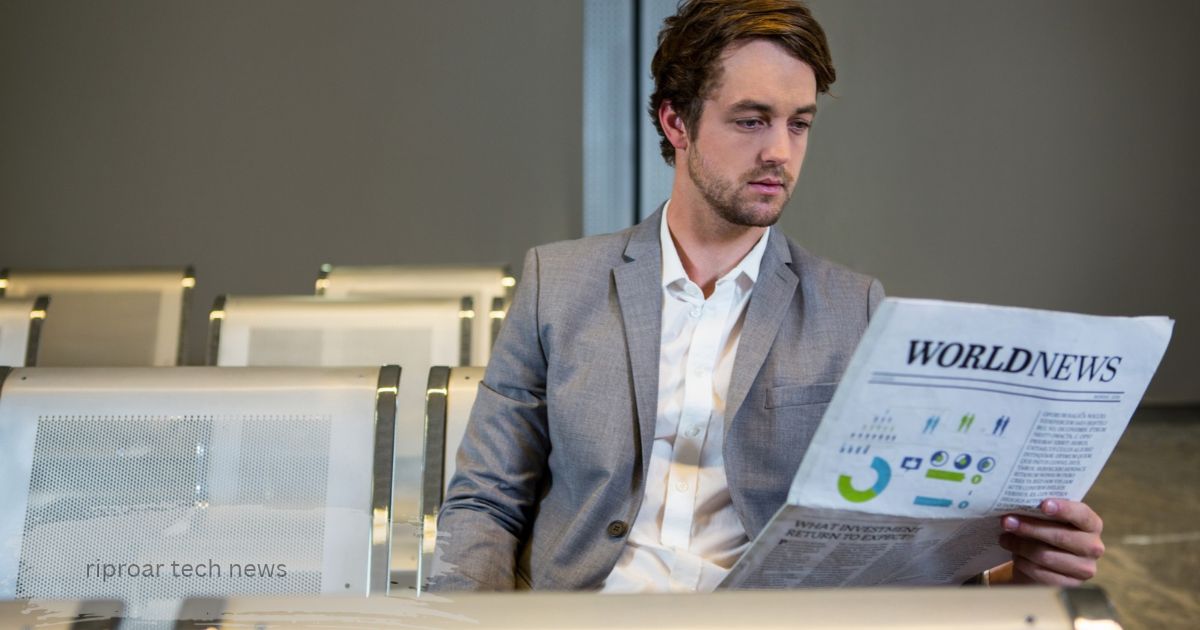 young man in a grey blazer reading a world riproar tech news  paper with charts while waiting, shown as a riproar tech updates visual