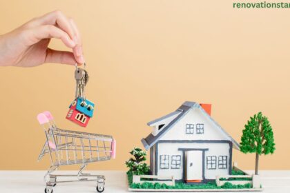 Hand holding keys with a miniature house keychain above a small shopping cart next to a model family home, symbolizing a competitive house for sale Saskatoon real estate market.