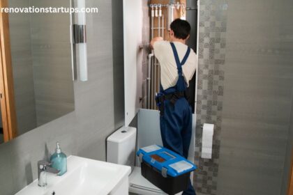 Plumber in blue overalls installing exposed pipes during a condo bathroom renovation, with a modern gray-tiled shower, white vanity sink, and toilet visible.