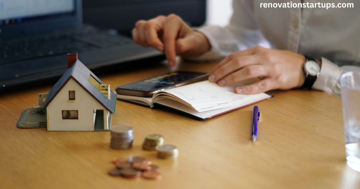 Person calculating cost of home renovation with calculator, notebook, small house model, and stacked coins on desk
