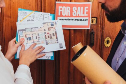 Real estate agent showing floor plan to buyer with a For Sale sign in the background — house for sale in Winnipeg