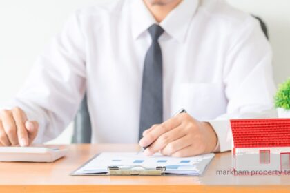 Man in white shirt calculating Markham property tax with calculator, documents, and house model on desk