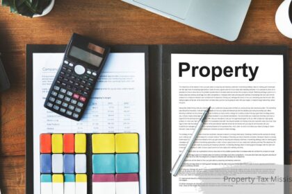 Flat-lay desk view featuring a calculator resting on financial documents, colorful index cards, a pen resting on a page titled "Property", and a coffee cup on a wooden table.