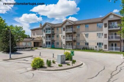 Three-storey beige apartment building at 10 East Ave with balconies, landscaped entrance, and paved parking lot
