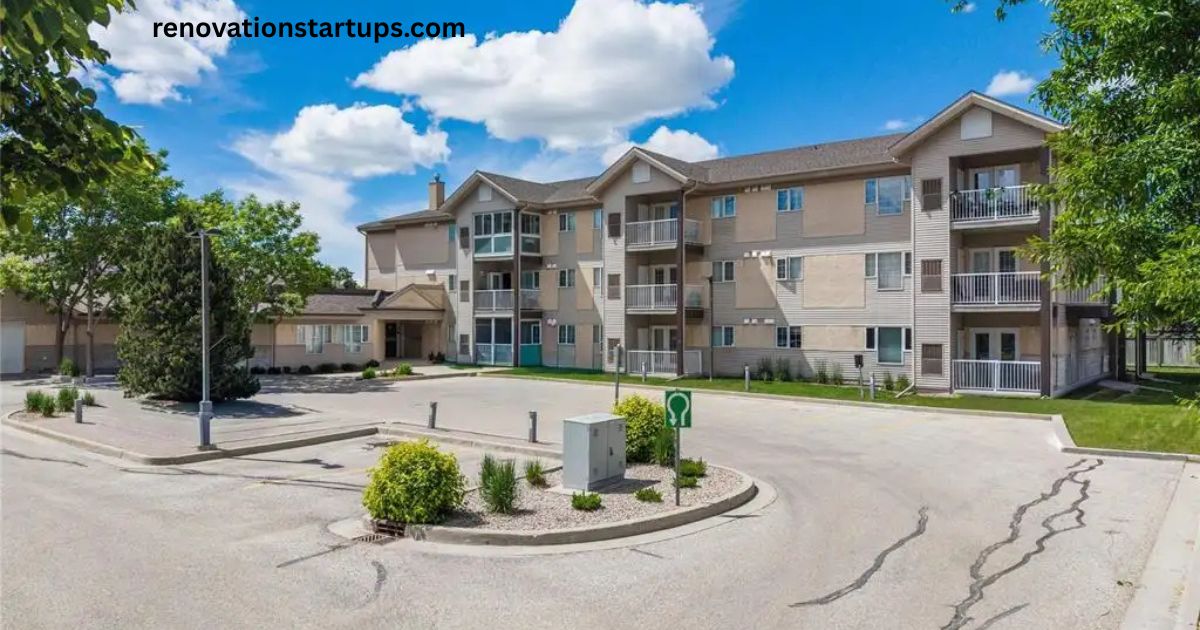Three-storey beige apartment building at 10 East Ave with balconies, landscaped entrance, and paved parking lot