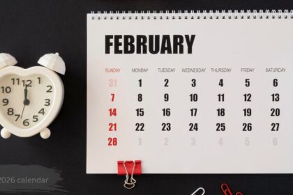 February 2026 calendar with spiral-bound page showing Sunday-start layout and a heart-shaped alarm clock beside it