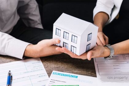 Two people holding a model house together over mortgage application and cps property documents on a desk