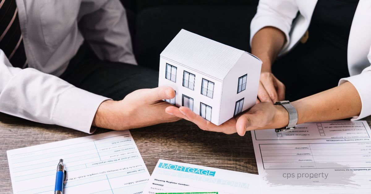 Two people holding a model house together over mortgage application and cps property documents on a desk