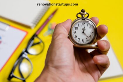Hand holding a vintage pocket watch symbolizing tiempo (time/weather), with a notebook, glasses, and a pie chart document blurred in the background — renovationstartups.com