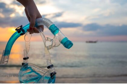 Snorkel mask and tube held up at sunset, symbolizing one of the best places to snorkel for a beach getaway