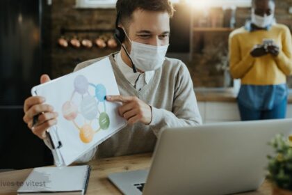 Woman wearing a face mask working on a laptop while researching alternatives to vitest, with a sticky note idea board in the background