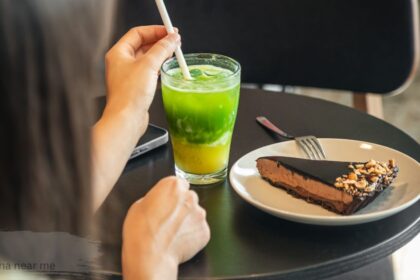 Two people whisking fresh matcha lattes with bamboo tools at a wooden cafe table