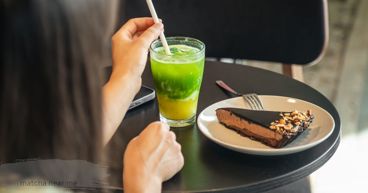 Two people whisking fresh matcha lattes with bamboo tools at a wooden cafe table