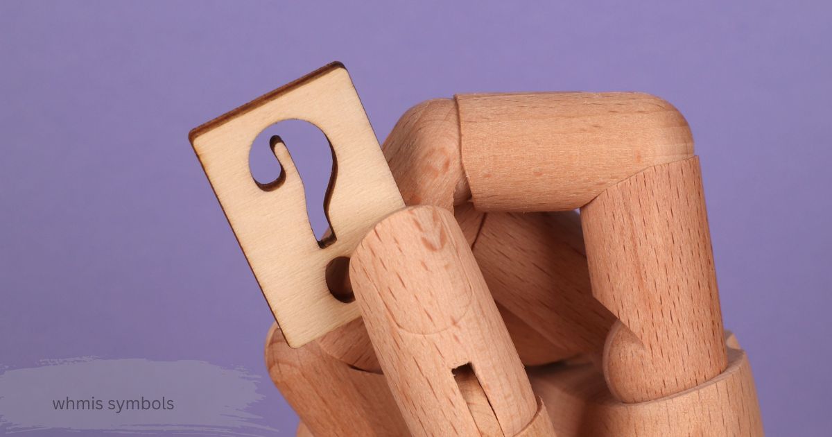 Wooden hand holding a question mark tag on a purple background to explain hazard pictograms
