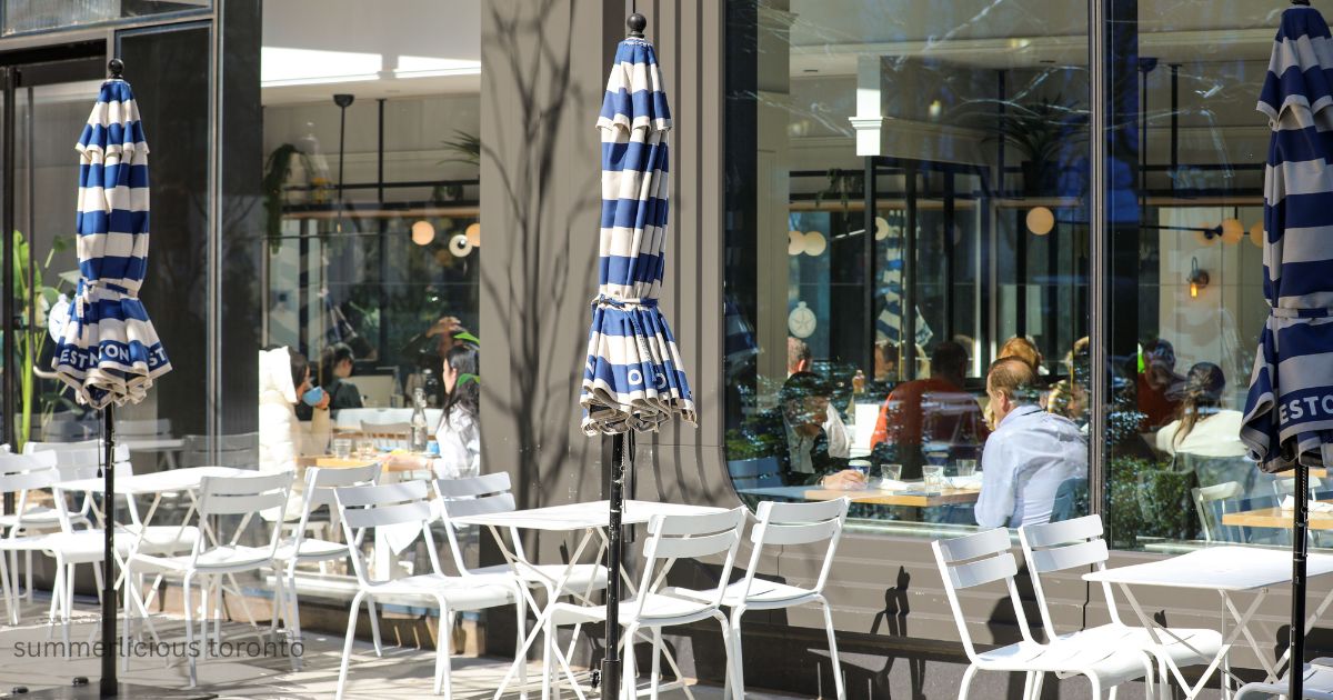 Outdoor patio seating with blue and white striped umbrellas at a restaurant during Summerlicious Toronto