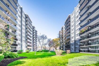 Two high rise apartment buildings with balconies facing a green courtyard lawn under a blue sky, a loft to rent in Toronto.
