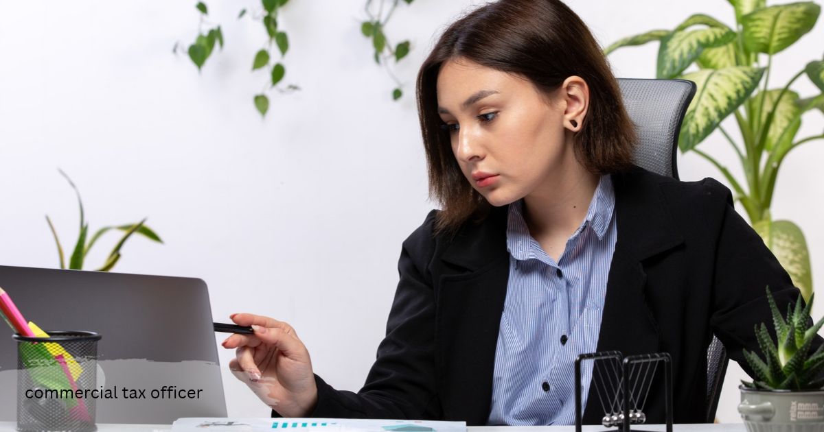 Young woman in a black blazer commercial tax officer reviewing business figures on her laptop while holding a pen at a desk with green plants nearby