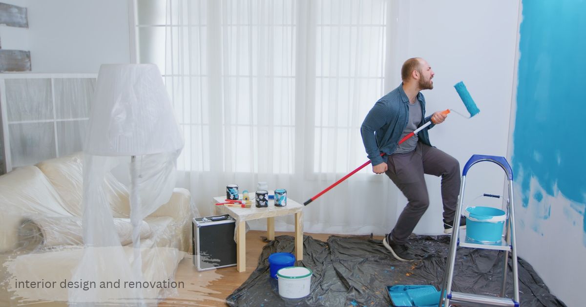Man painting a living room wall interior design and renovation with a blue roller while furniture is covered in plastic sheets during home renovation