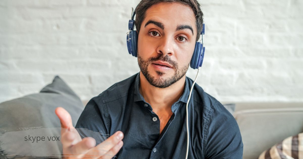 Bearded man wearing blue headphones and gesturing with his hand in front of a white brick wall skype vox