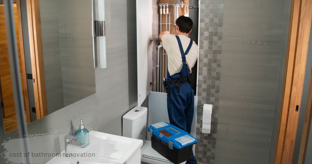 Plumber in blue overalls fixing pipes behind a wall panel in a modern grey bathroom, showing cost of bathroom renovation the labour side of bathroom renovation cost