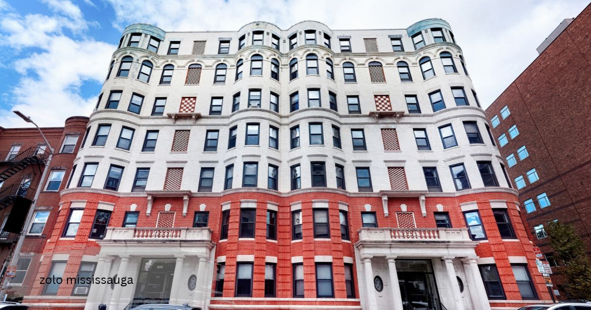 Historic apartment building zolo mississauga with a white and red brick facade, curved bay windows, and stone balconies under a bright blue sky